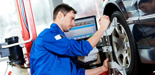 Cómo montar un taller de alineación y balanceo de automóviles Hombre haciendo mantenimiento a un neumático en un taller de mecánica