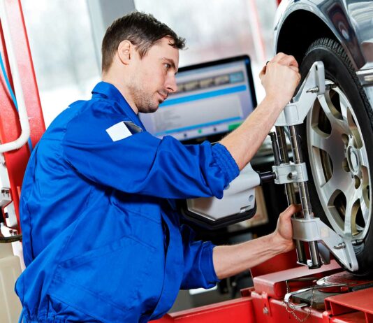 Cómo montar un taller de alineación y balanceo de automóviles Hombre haciendo mantenimiento a un neumático en un taller de mecánica