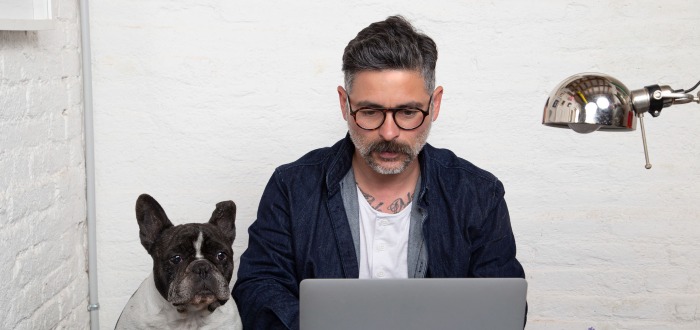 Hombre trabajando en su ordenador portátil junto a su perro.