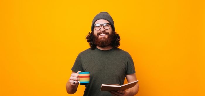 Hombre con una taza y un libro en una mano como ejemplo de geek