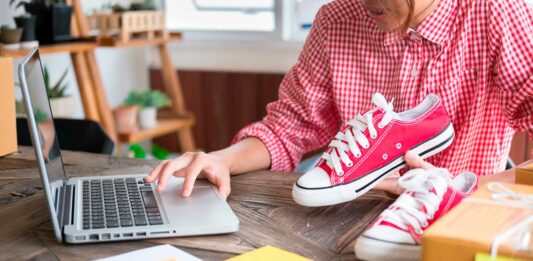 Productos para revender rentables | Todo lo que debes saber para hacerlo con éxito persona sosteniendo tennis sobre una mesa mientras opera un computador