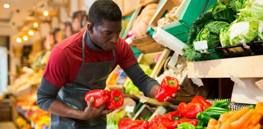 Cómo montar una tienda de barrio | Paso a paso y 7 ideas de qué locales poner hombre en tienda de barrio acomodando unos pimentones