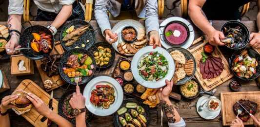 Comidas para vender | Empieza tu propio negocio culinario Mesa de comida con platos llenos. Se ven las manos de la gente compartiendo.