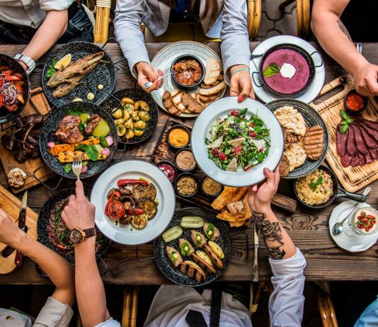 Comidas para vender | Empieza tu propio negocio culinario Mesa de comida con platos llenos. Se ven las manos de la gente compartiendo.