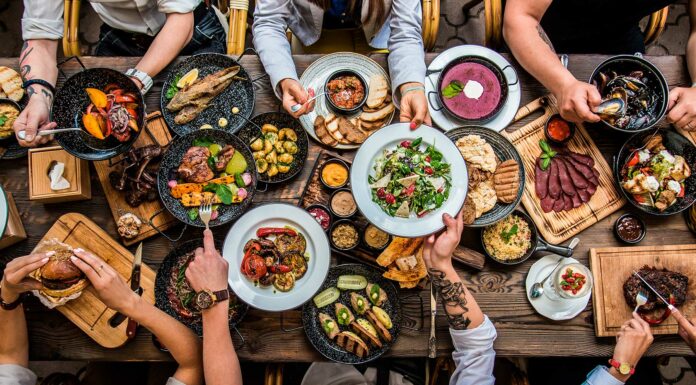 Comidas para vender | Empieza tu propio negocio culinario Mesa de comida con platos llenos. Se ven las manos de la gente compartiendo.