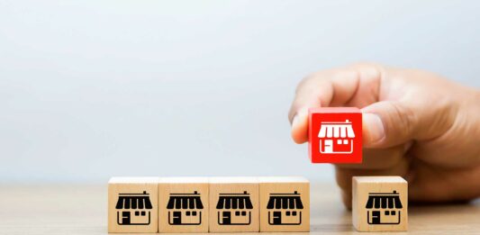 Franquicias «Low Cost» | Las mejores y más baratas opciones en el mercado para invertir Cajitas pequeñas con íconos de franquicias alineadas. Una mano levanta una de ellas.