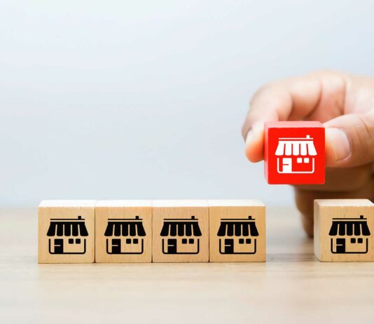 Franquicias «Low Cost» | Las mejores y más baratas opciones en el mercado para invertir Cajitas pequeñas con íconos de franquicias alineadas. Una mano levanta una de ellas.