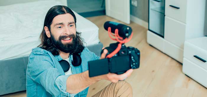 Un hombre barbudo y expresivo sostiene una cámara con micrófono para ganar dinero en Youtube